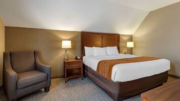 A hotel room with a large bed, a chair, a nightstand, and two wall lamps.