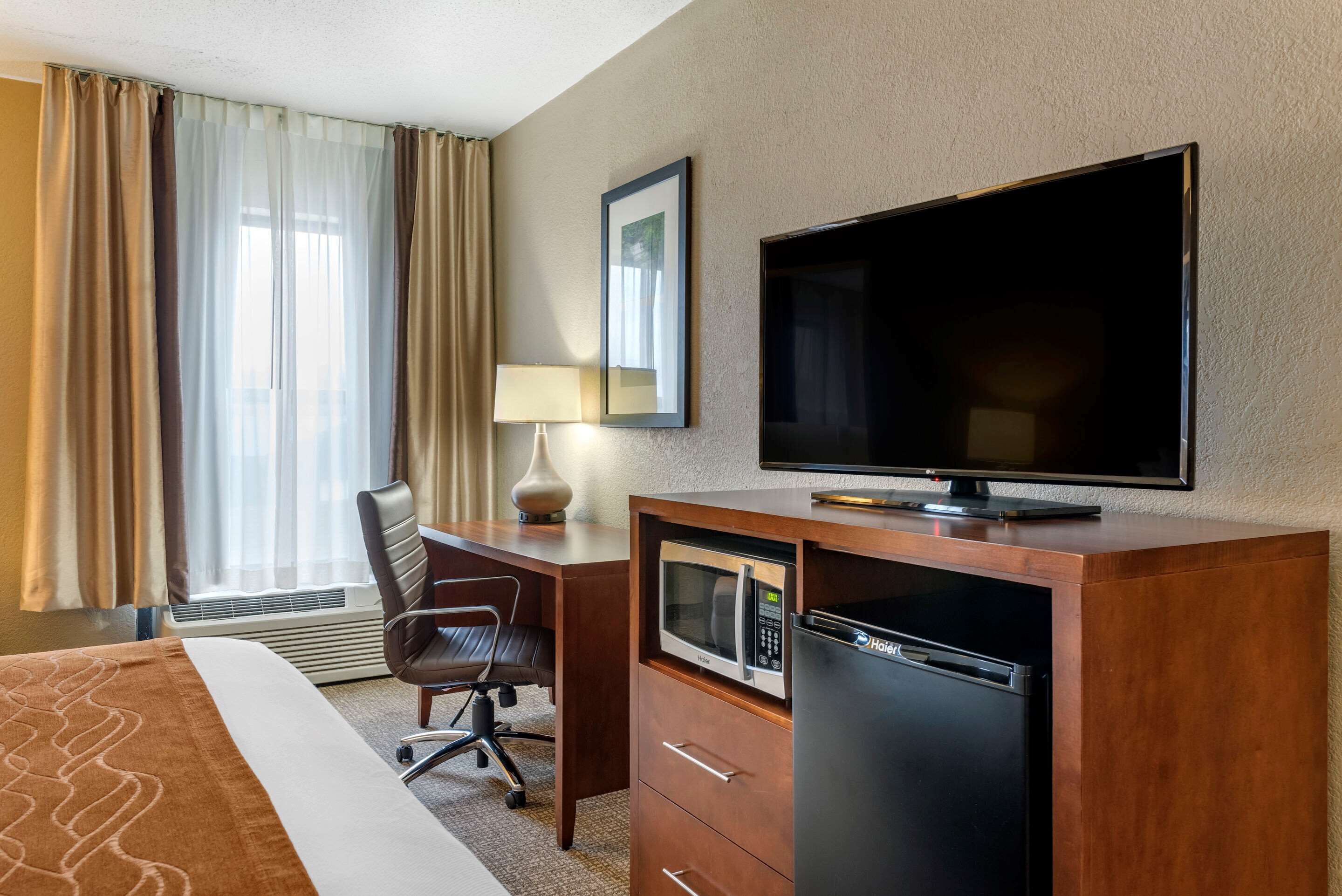 A hotel room with a bed, a desk with a computer, a television, a microwave, and a refrigerator.