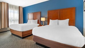 A hotel room with two beds, a nightstand, a lamp, and a window with curtains.