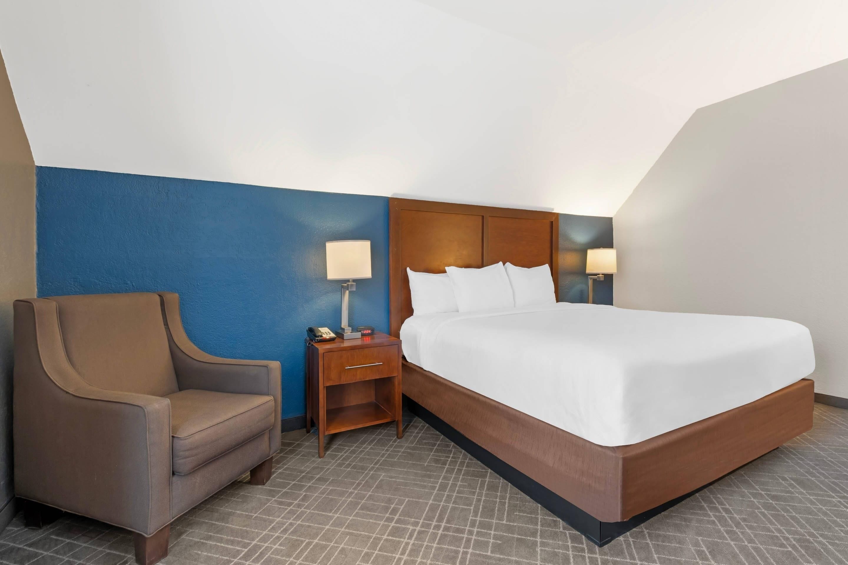 A hotel room with a bed, a chair, a nightstand, and two lamps.