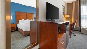 A hotel room with a bed, a desk with a television, a chair, and a window with curtains.