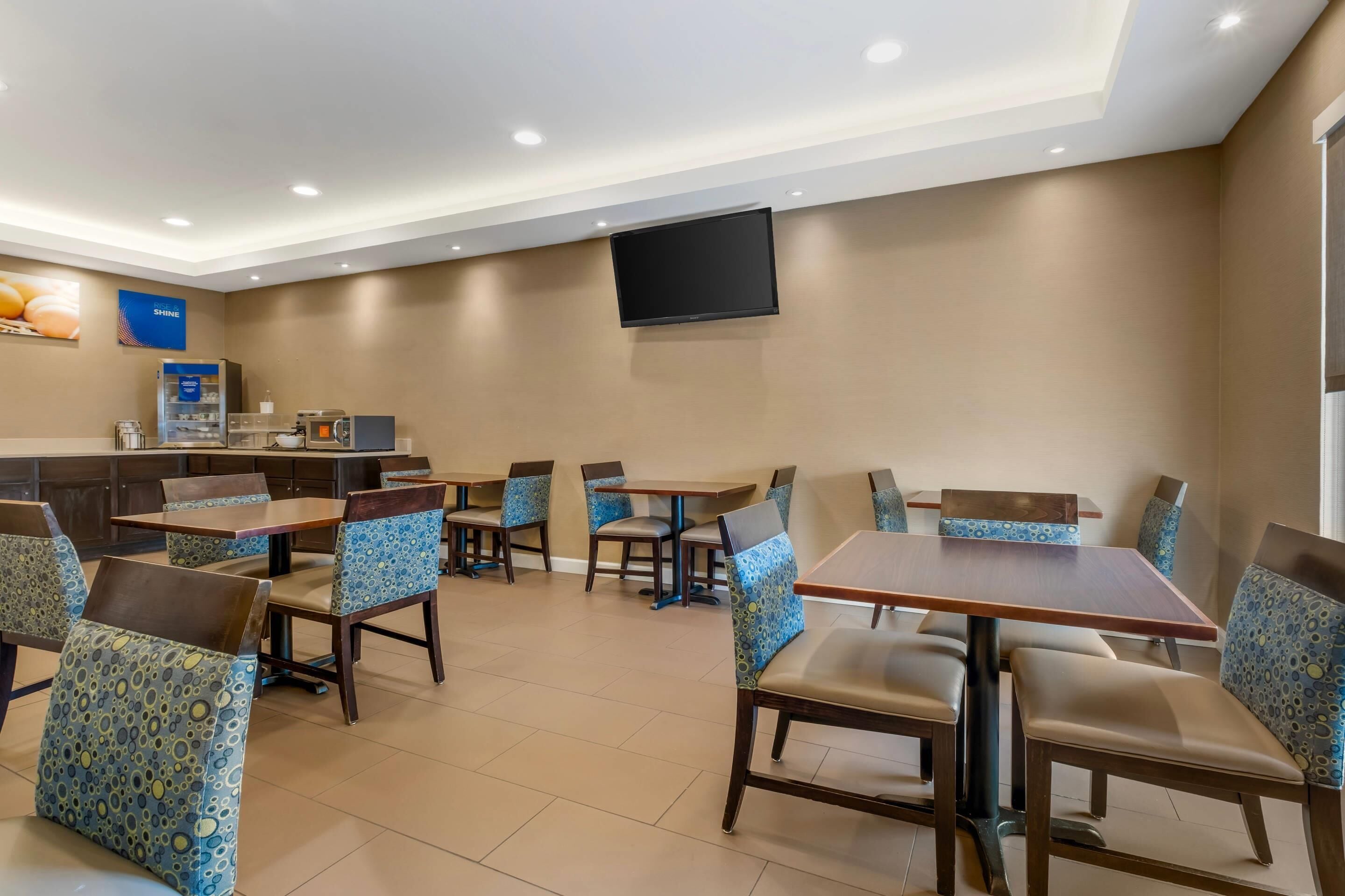 Un comedor de hotel con mesas, sillas, un televisor de pantalla plana y una cafetera.