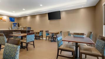 A hotel dining area with tables and chairs, a flat-screen TV, and a coffee machine.