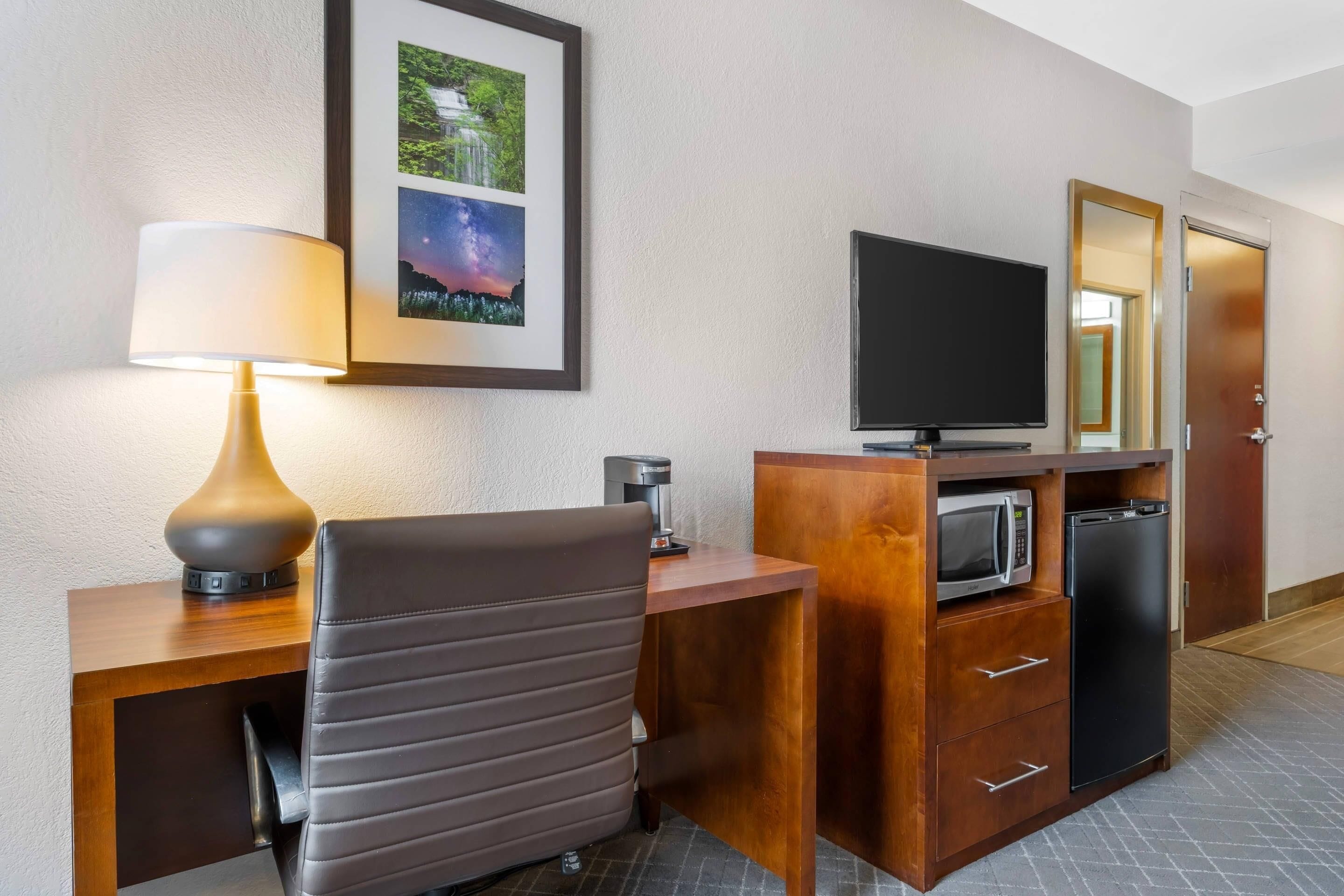 Habitación de hotel con escritorio, silla, lámpara, televisor, microondas y refrigerador.