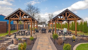 A covered outdoor seating area with picnic tables and benches, surrounded by landscaped gardens and trees.