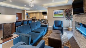 A modern hotel lobby with a blue sofa, a fireplace, a television, and a dining area.