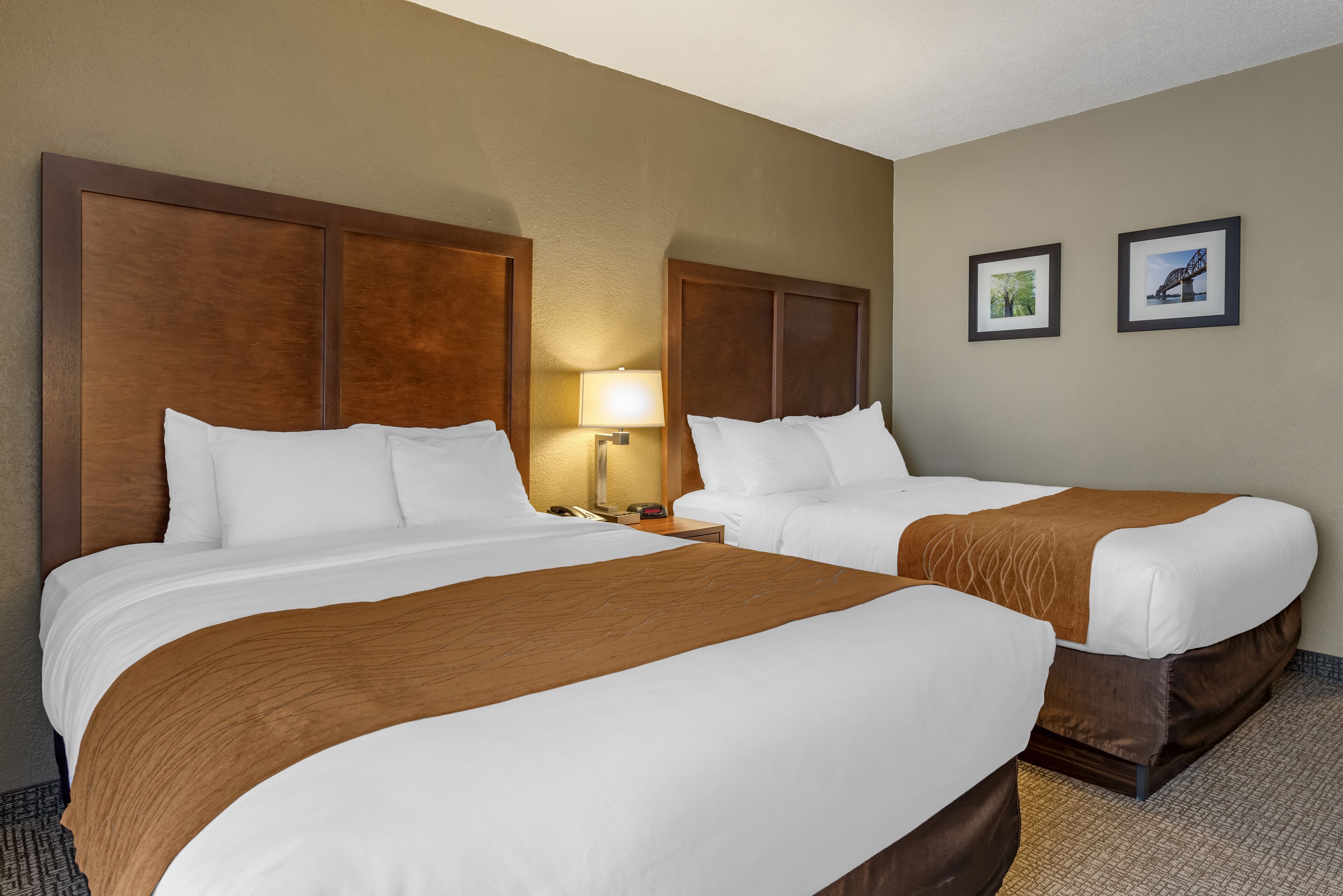 A hotel room with two beds, a nightstand, a lamp, and two framed pictures on the wall.