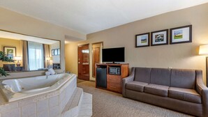 A hotel room with a large bathtub, a sofa, a television, and framed pictures on the wall.
