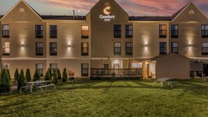 A Comfort Inn hotel with a well-lit exterior, a covered outdoor seating area, and a grassy lawn.