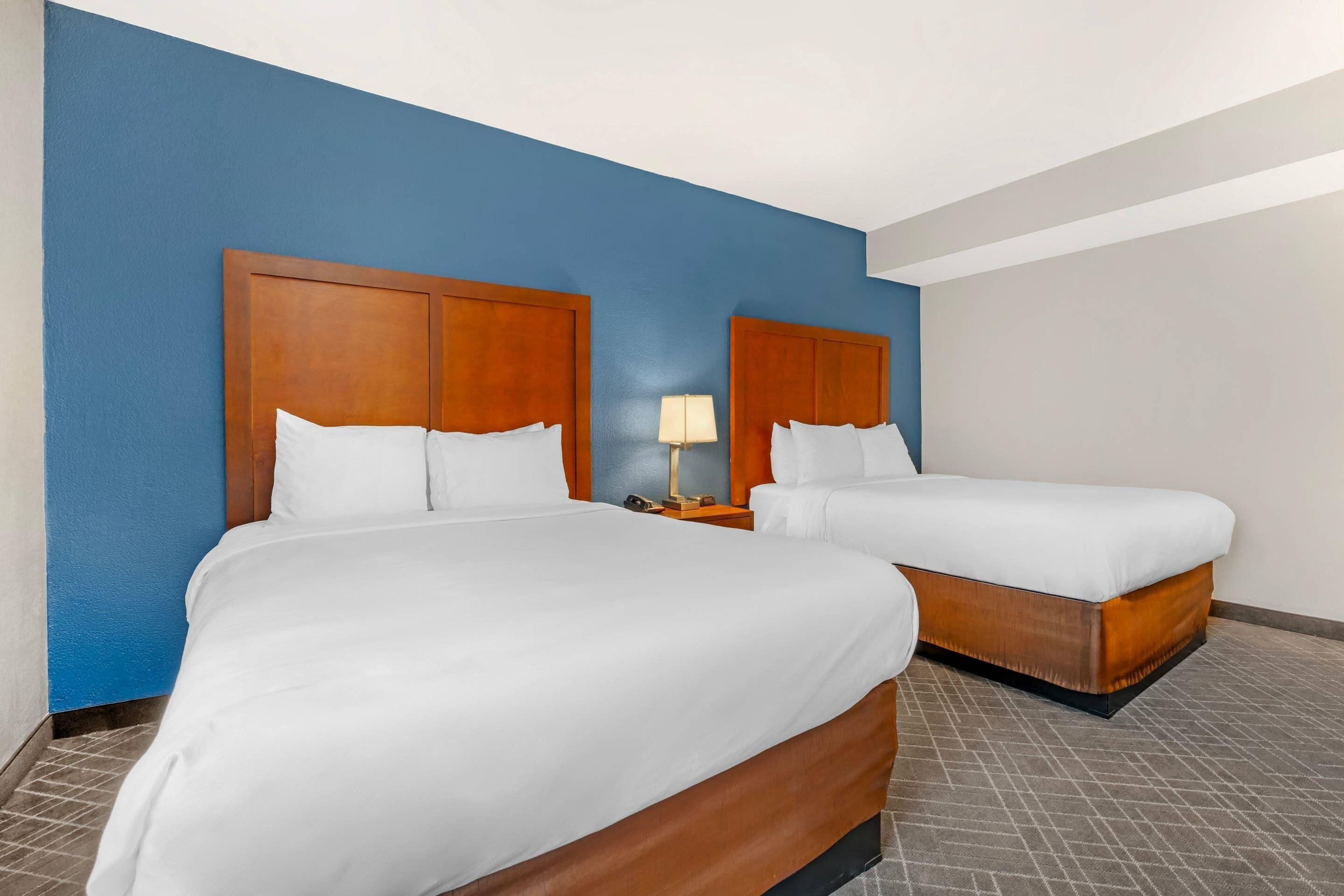 A hotel room with two beds, a nightstand with a lamp, and a blue accent wall.