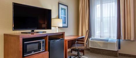 Une chambre d’hôtel équipée d’une télévision, d’un four à micro-ondes, d’un mini-réfrigérateur, d’un bureau, d’une chaise, de la climatisation et d’une fenêtre avec des rideaux.