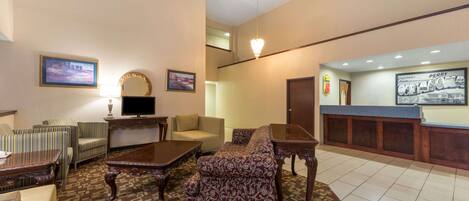 A hotel lobby with a sofa, armchairs, a television, and a reception desk.