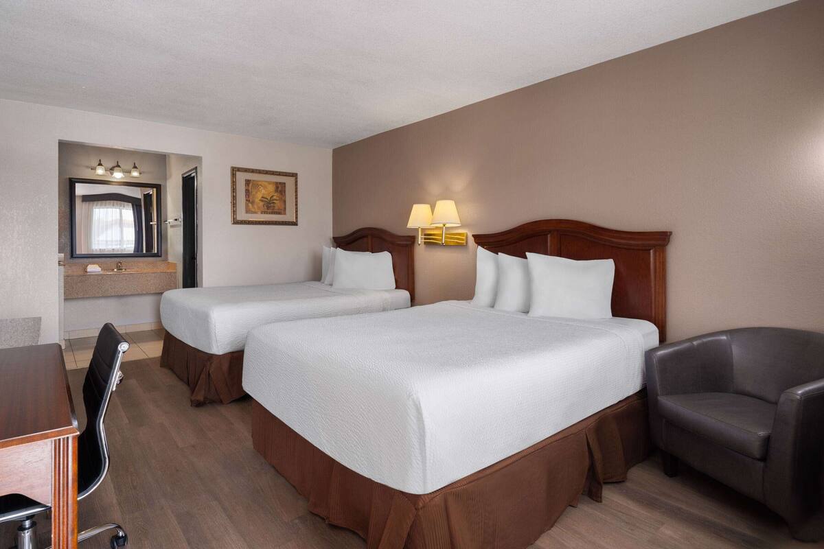 Une chambre d’hôtel avec deux lits, un bureau, une chaise, un miroir et une lampe fixée au mur.