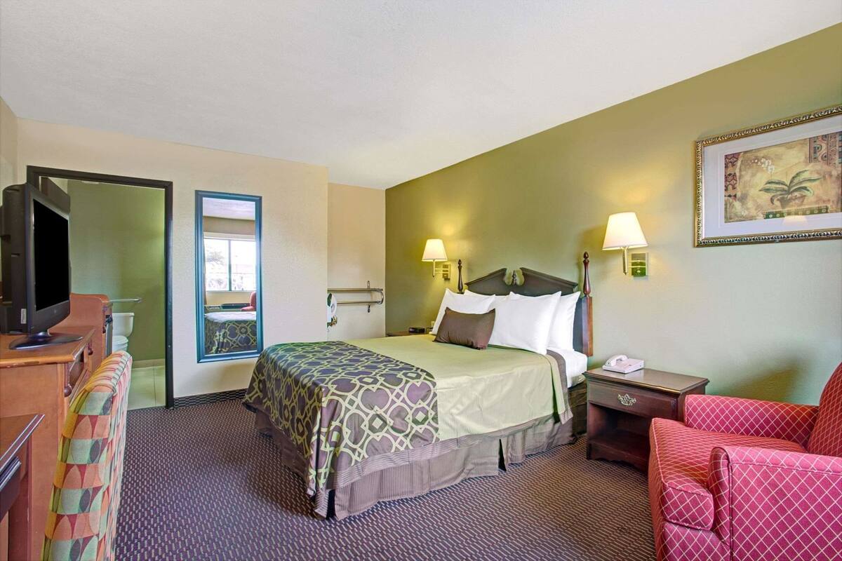 Une chambre d’hôtel avec un lit, une table de chevet, une chaise, une télévision et une porte de salle de bain.