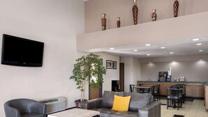 A modern hotel lobby with a grey leather sofa, a small table, and a TV mounted on the wall. - Travelodge by Wyndham Tucson AZ (Tucson)