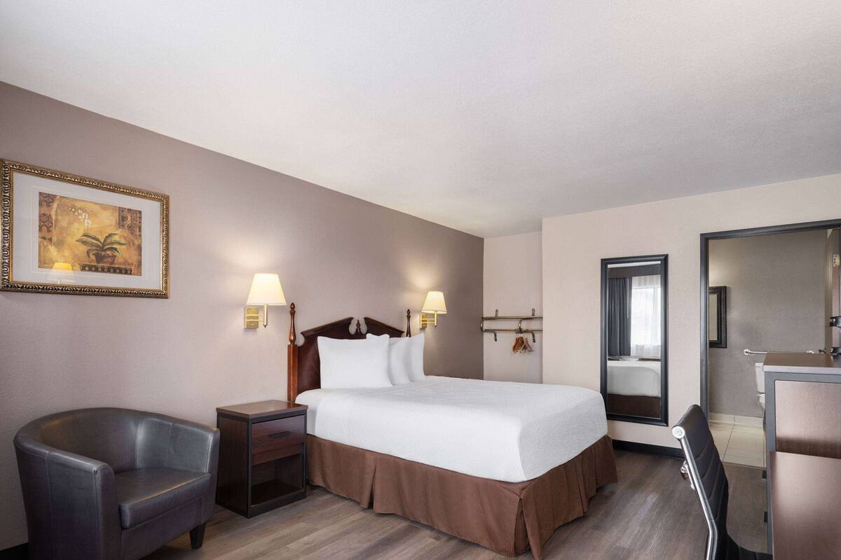 Une chambre d’hôtel comprenant un lit, des lampes de chevet, une chaise, une commode et un miroir.