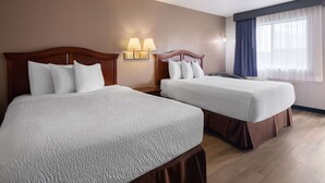 A hotel room with two beds, a nightstand, a lamp, and a window with curtains. - Travelodge by Wyndham Tucson AZ (Tucson)