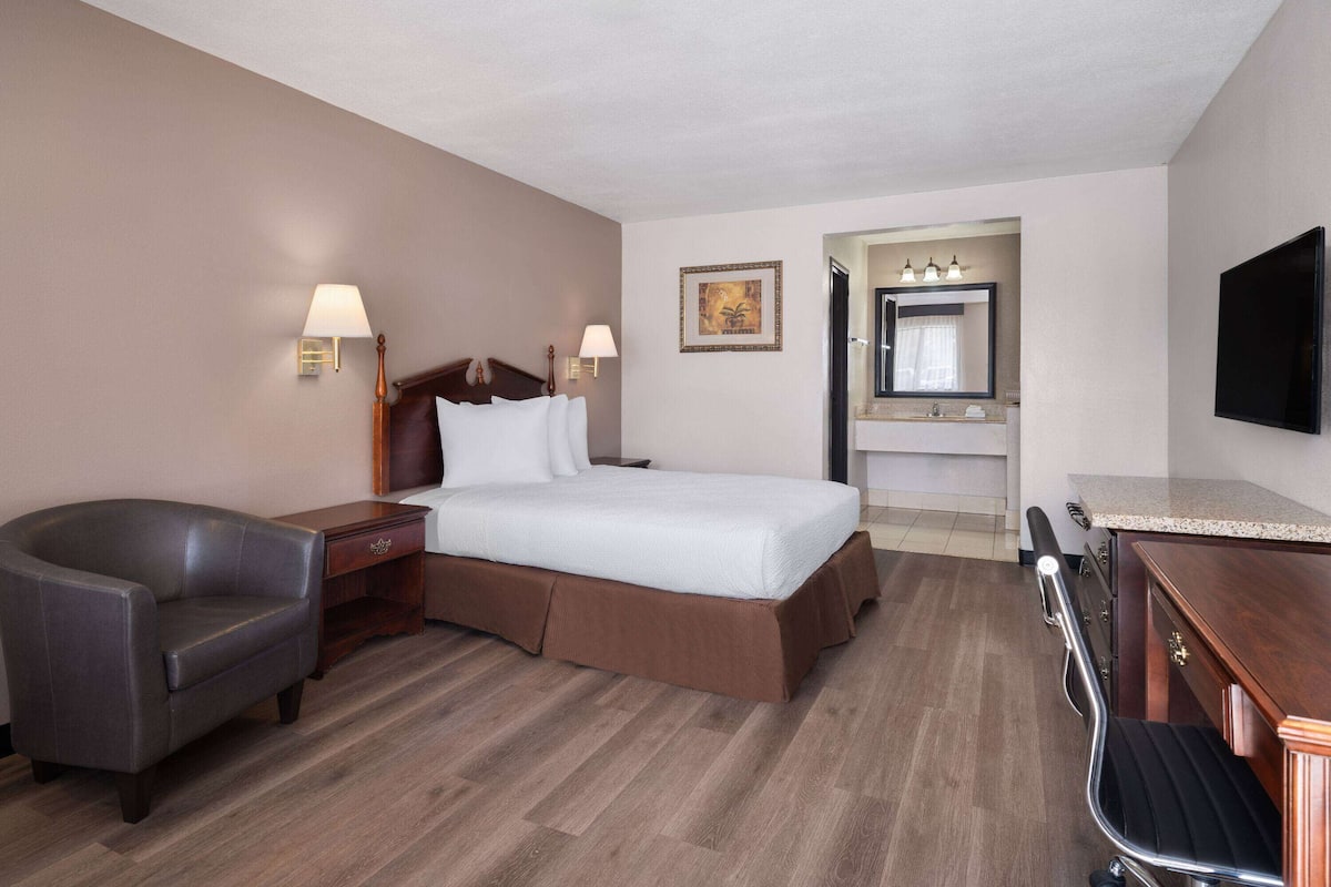 Une chambre d’hôtel avec un lit, un bureau, une chaise, une télévision et une salle de bain visible à travers une porte ouverte.