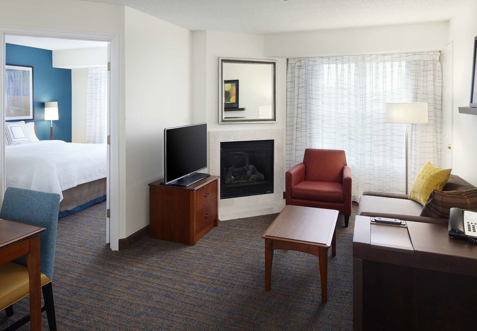 A hotel room with a bed, TV, fireplace, armchair, sofa, and a desk with a phone.
