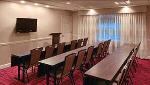 A conference room with a long table and chairs, a TV mounted on the wall, and a window with curtains. - Residence Inn by Marriott St Louis Airport (Earth City)