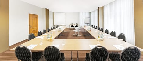 Una sala de conferencias con una mesa larga, sillas, una pantalla de proyector y una pizarra.