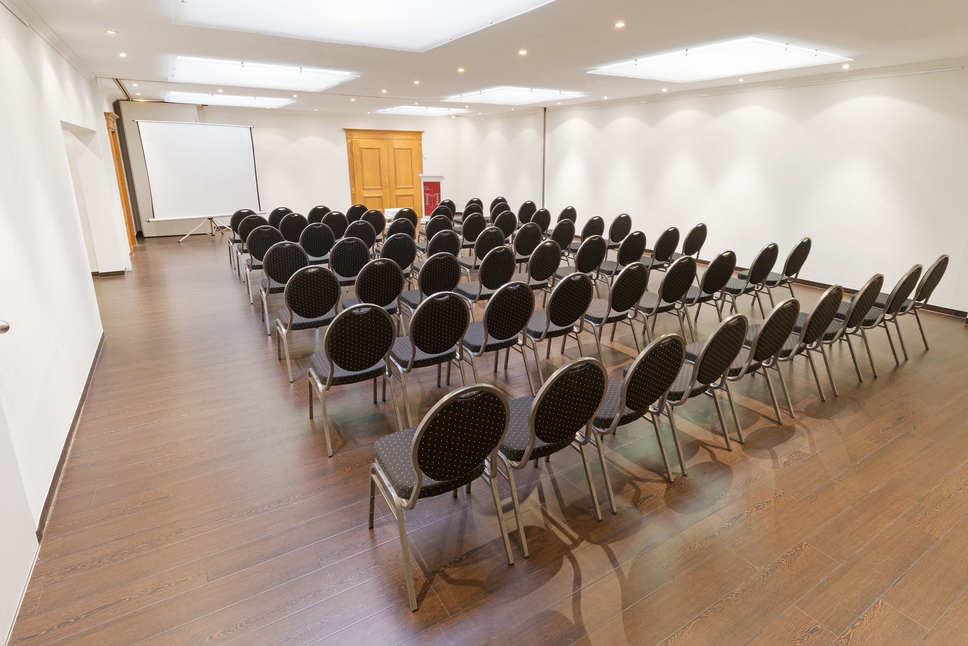 A conference room with rows of chairs, a whiteboard, and a podium.