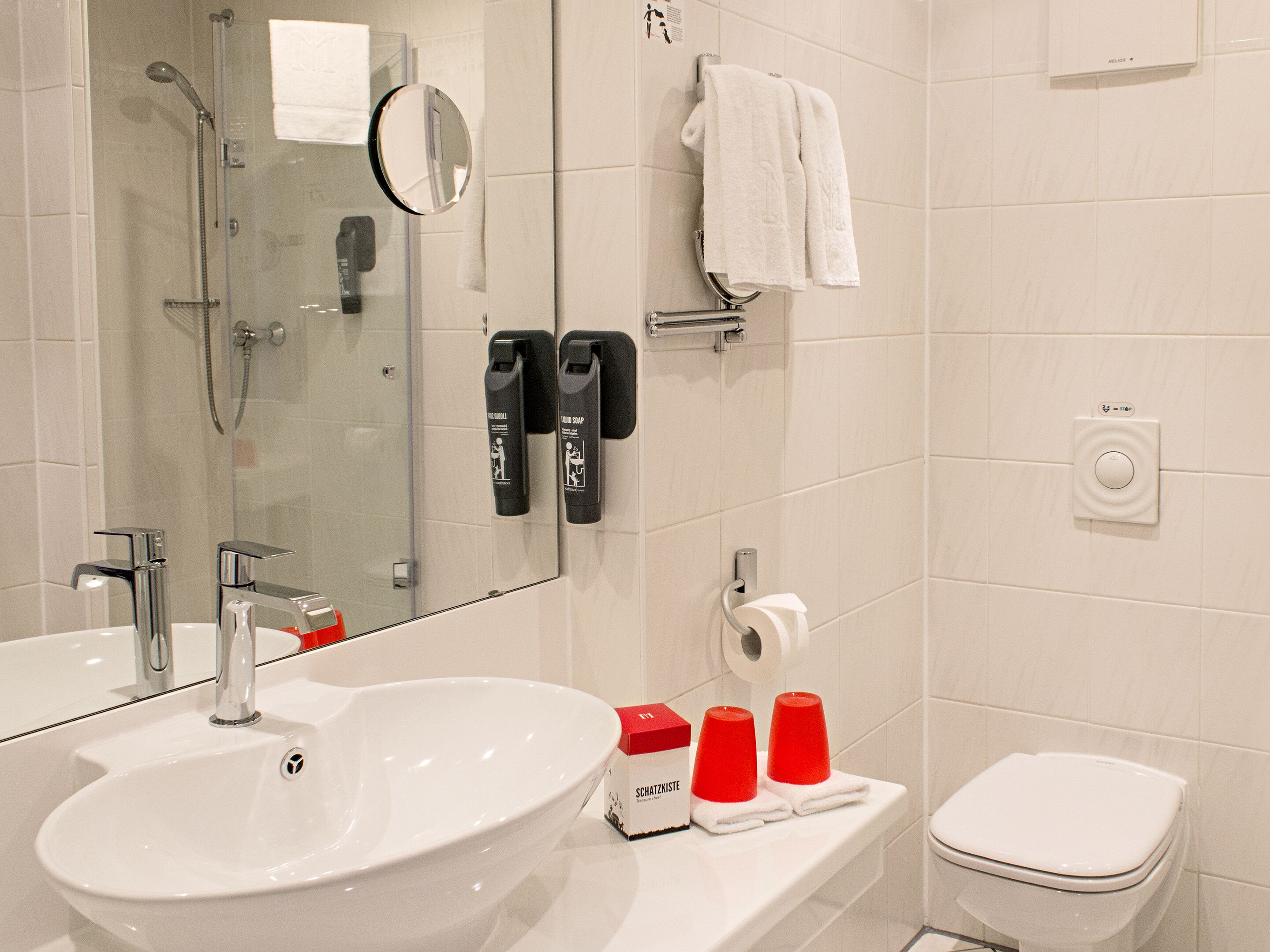 Un bagno moderno con un lavandino capiente, uno spazio doccia in vetro, un portasciugamani con due asciugamani e un water.