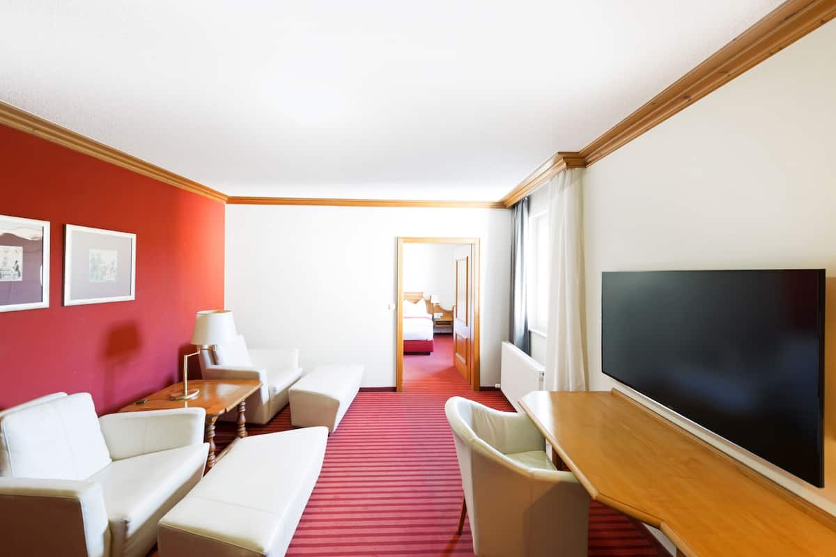 Hotellihuone, jossa on punainen matto, valkoiset huonekalut, televisio ja seinällä olevia tauluja.