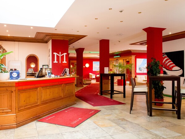 A hotel lobby with a reception desk, red accents, and a large shoe artwork on the wall. - Dormero Hotel Plauen (Plauen)