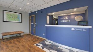 A reception area with a blue wall, a clock, a digital display, and a map on the wall. - Travelodge Aberdeen Bucksburn (Aberdeen)