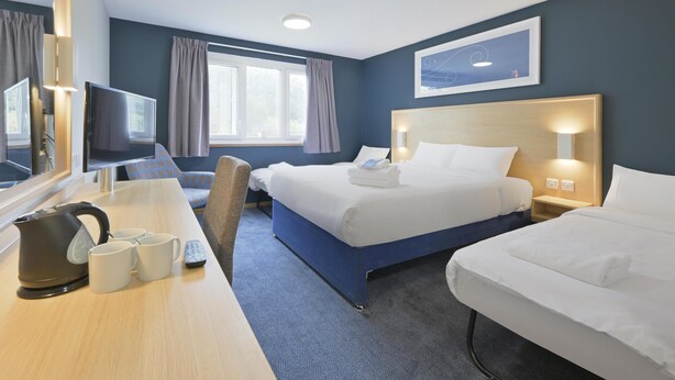 A hotel room with two beds, a desk with a television, a kettle, and mugs. - Travelodge Aberdeen Bucksburn (Aberdeen)