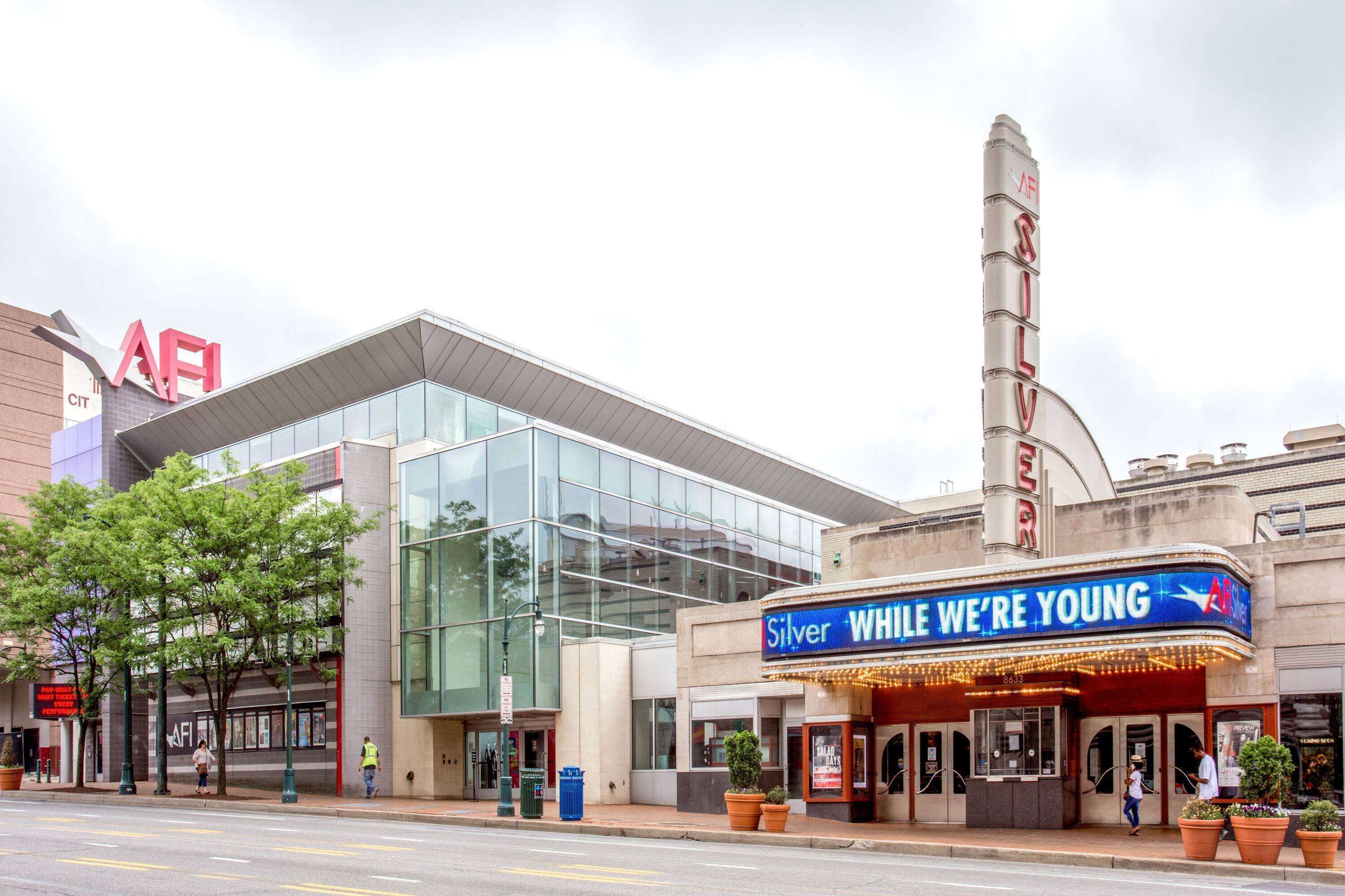 Un teatro con fachada de vidrio moderna y un cartel que dice 'Silver While We're Young'.