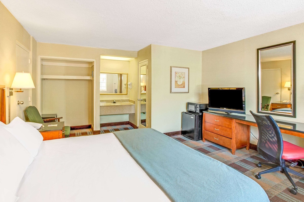 A hotel room with a bed, a desk with a computer, a television, a microwave, and a closet.