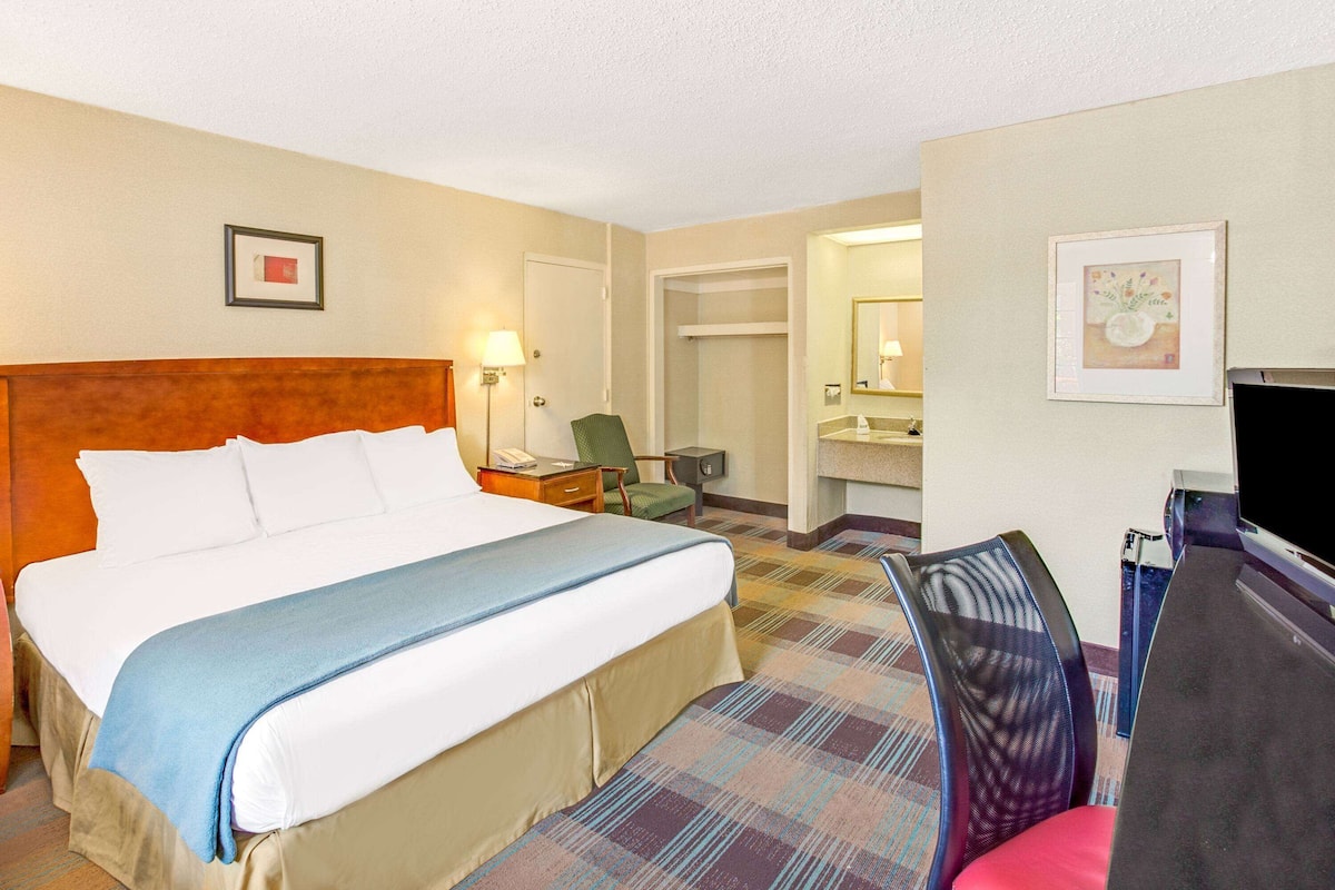 A hotel room with a large bed, a desk with a chair, a television, and a bathroom visible through an open door.