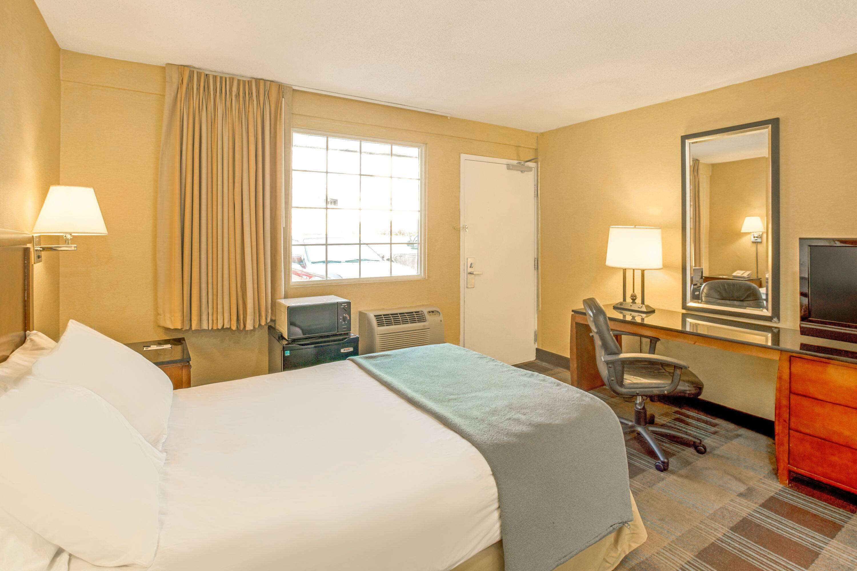 A hotel room with a bed, desk, chair, television, and a window with curtains.