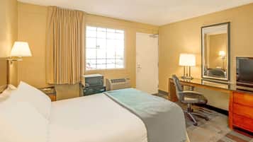 A hotel room with a bed, desk, chair, television, and a window with curtains.