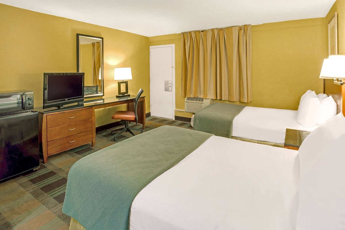 A hotel room with two beds, a desk with a TV, a dresser, and a mirror.