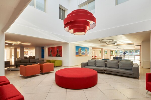 Un vestíbulo amplio con una zona de estar circular roja en el centro, varios sofás y una lámpara colgante roja de gran tamaño.