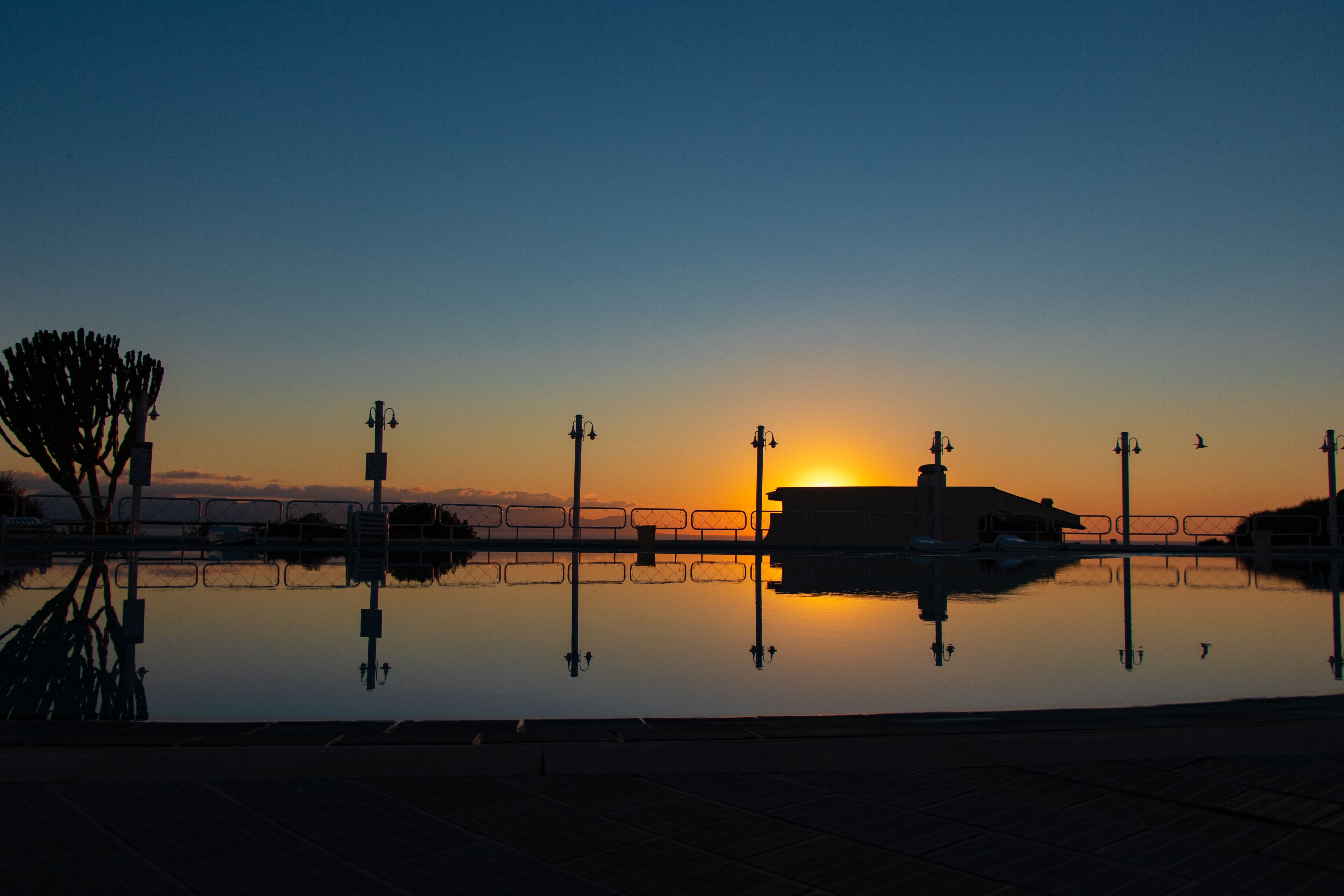 Ein Sonnenuntergang über ruhigem Wasser mit einer Brücke und Laternen.