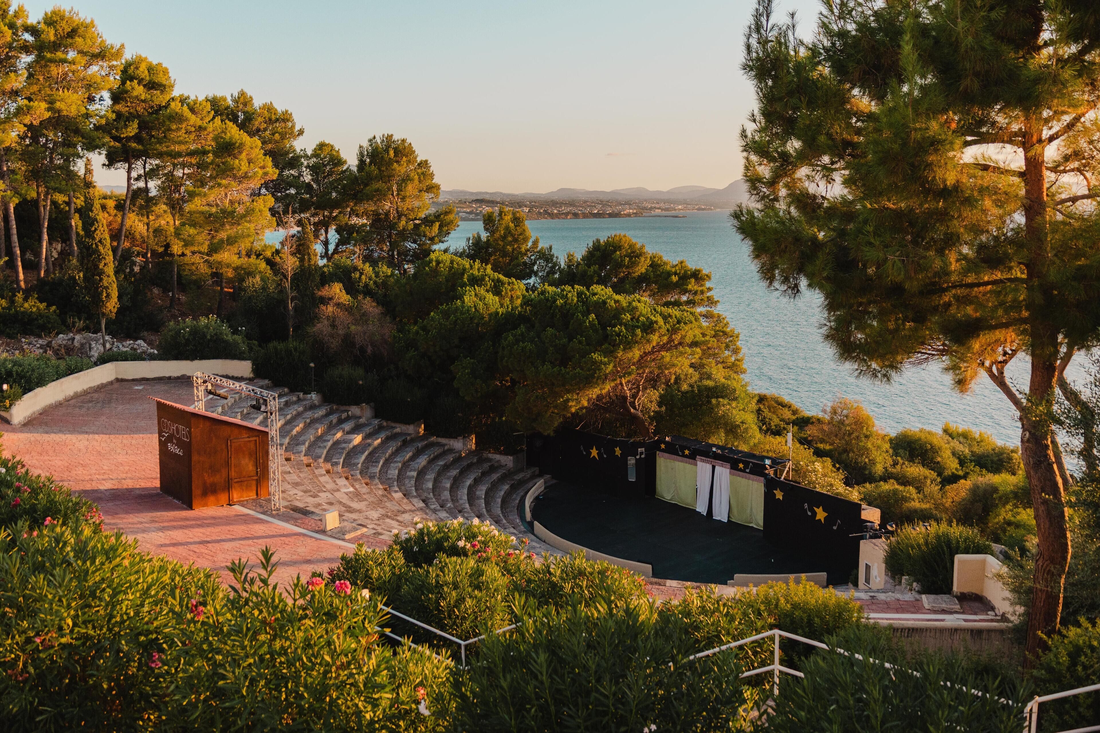 A theater with a stage, seating, and a backdrop of trees and water.