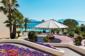 A resort pool area with a covered seating area, palm trees, and a view of the sea. - CDSHotels Terrasini - Città del Mare (Terrasini)