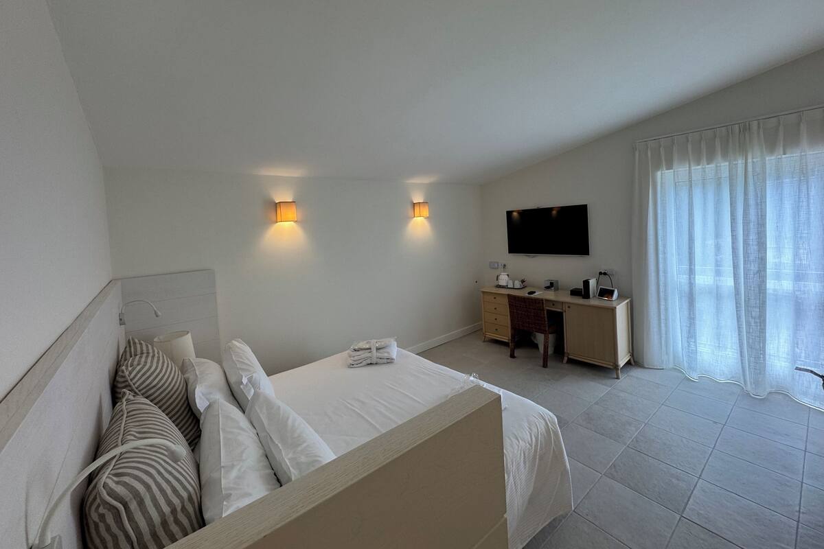 A hotel room with a bed, a desk, a chair, a television, and a window with curtains.