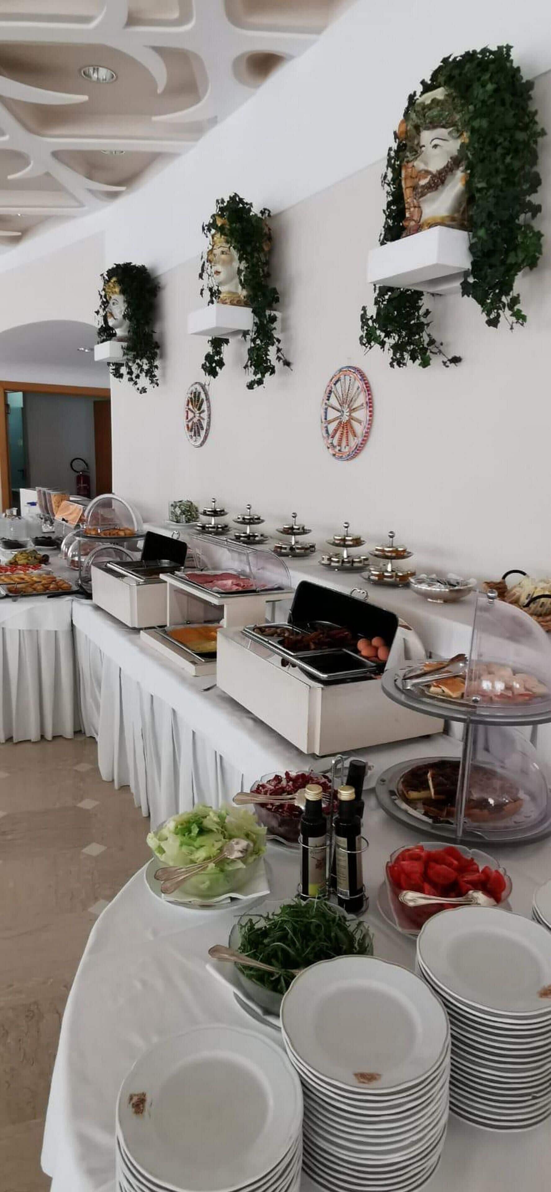 Un buffet proposant différents stands de nourriture, notamment un bar à salades et un stand de viandes, avec des tables blanches et un plafond orné de motifs géométriques.