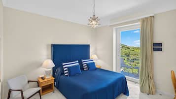 A bedroom with a large bed, two bedside tables with lamps, a chair, and a view of a balcony.