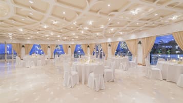 Un salón de banquetes con mesas redondas, sillas blancas y candelabros.