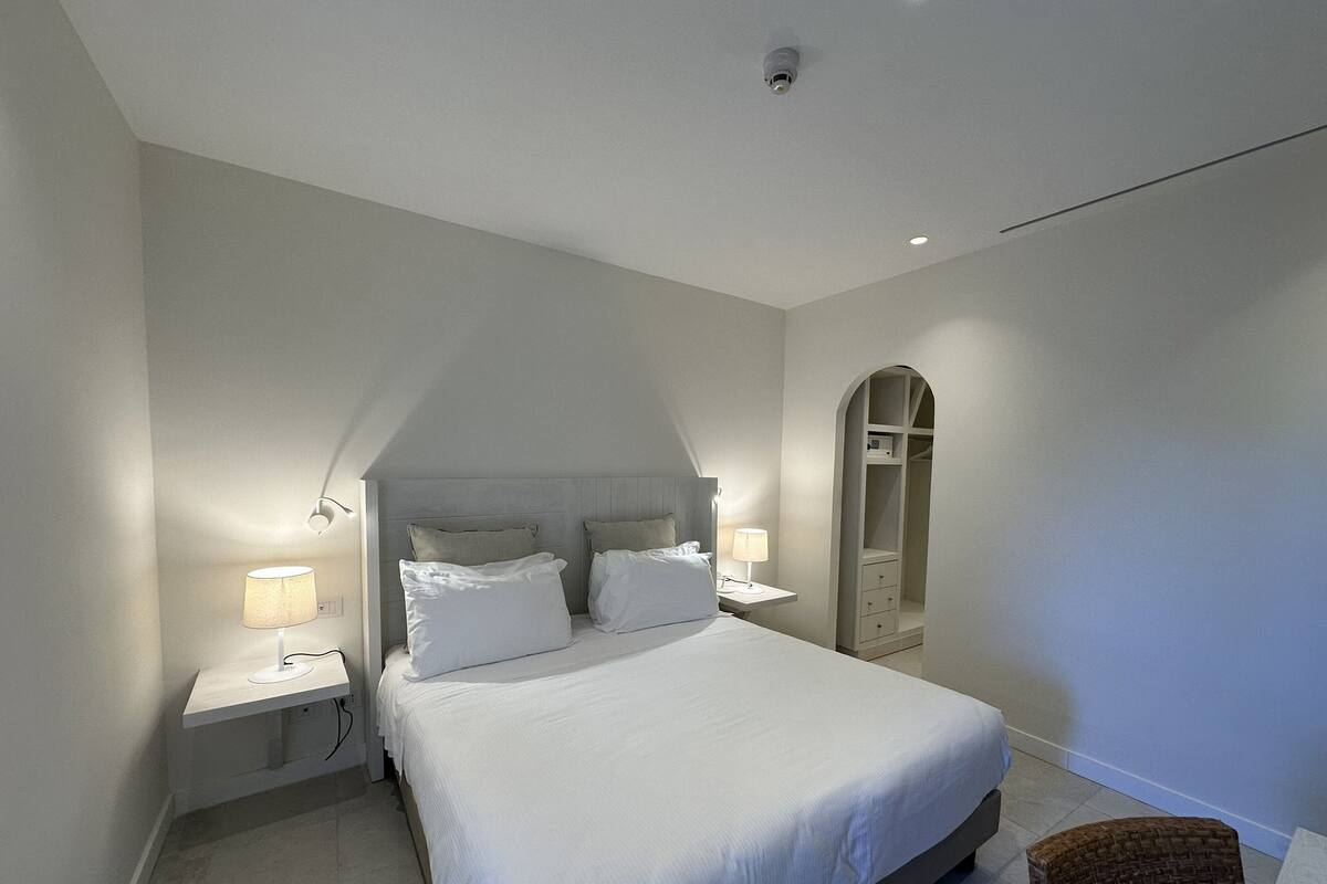 A bedroom with a large bed, two bedside tables with lamps, a wardrobe, and a small chair.