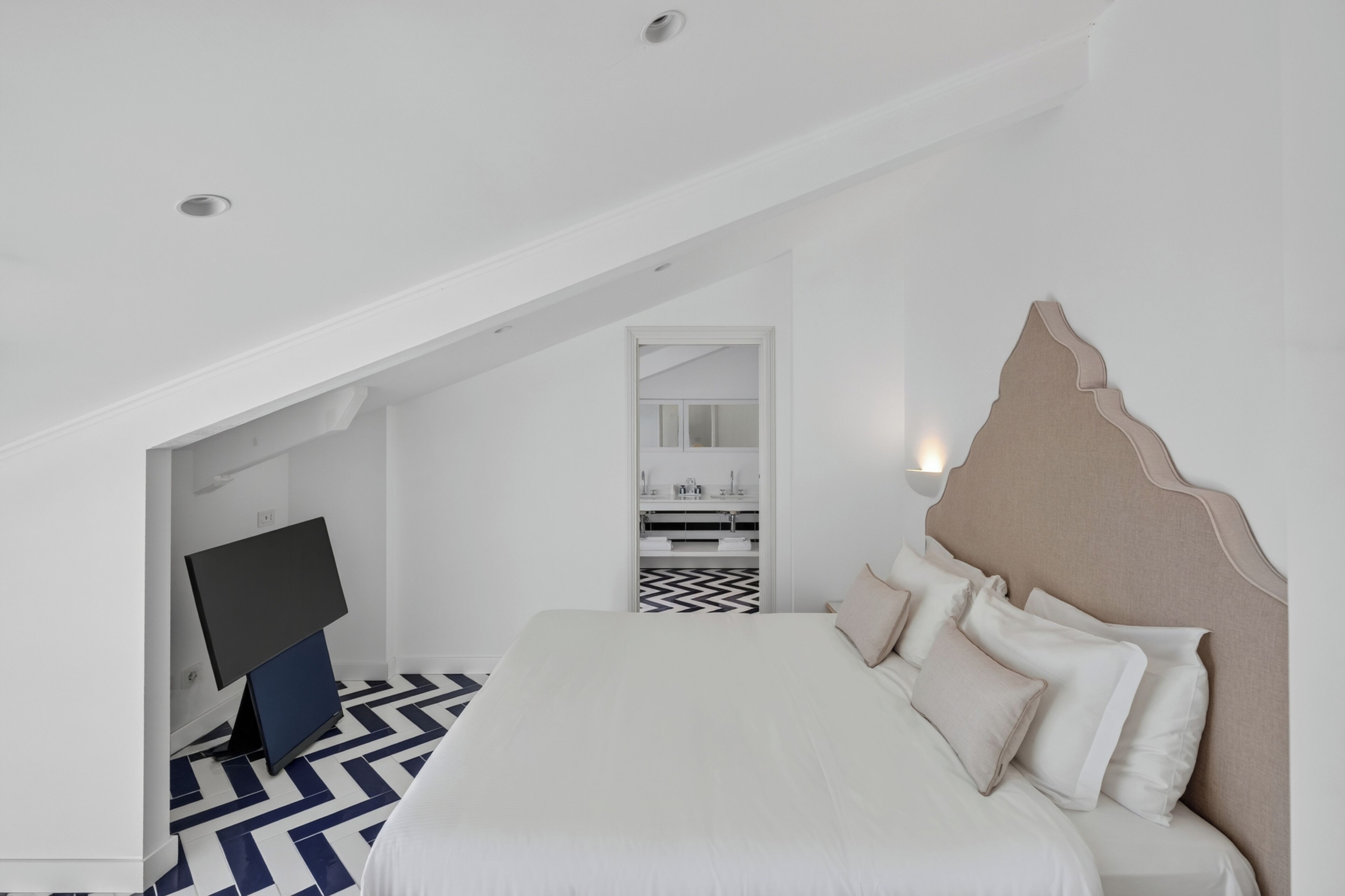 Une chambre d’hôtel moderne dotée d’un grand lit, d’un téléviseur à écran plat et d’une salle de bain visible à travers une porte ouverte.