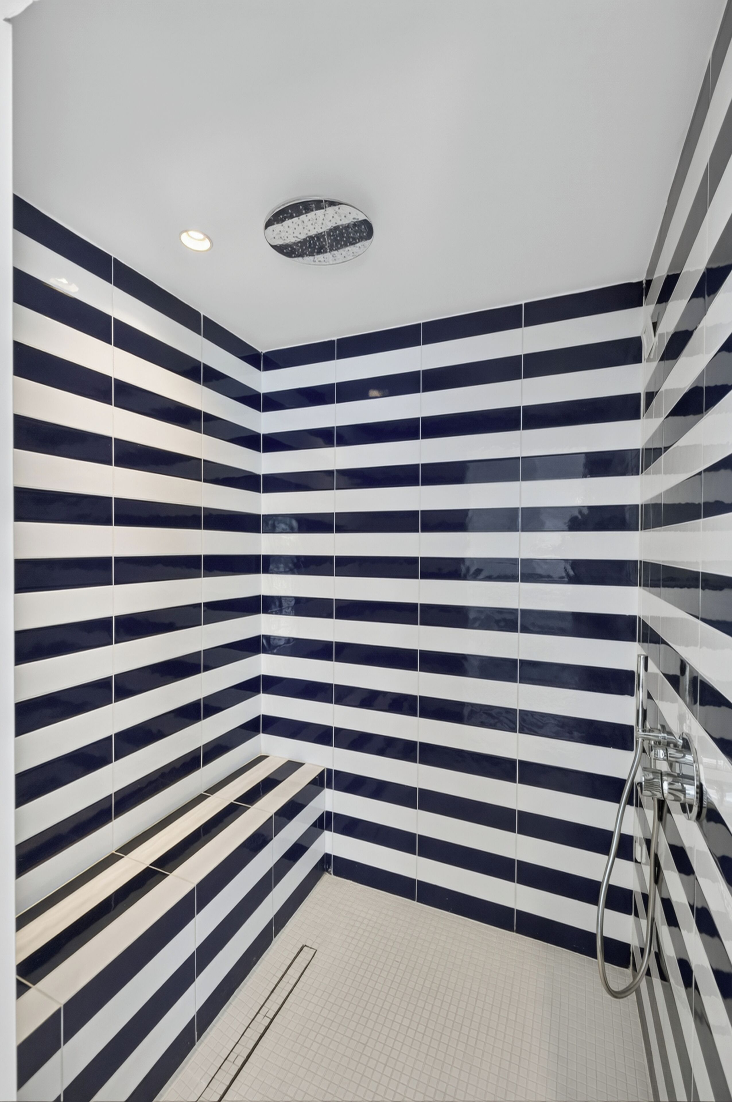 A bathroom with striped tile walls, a shower area, and a visible ceiling light.
