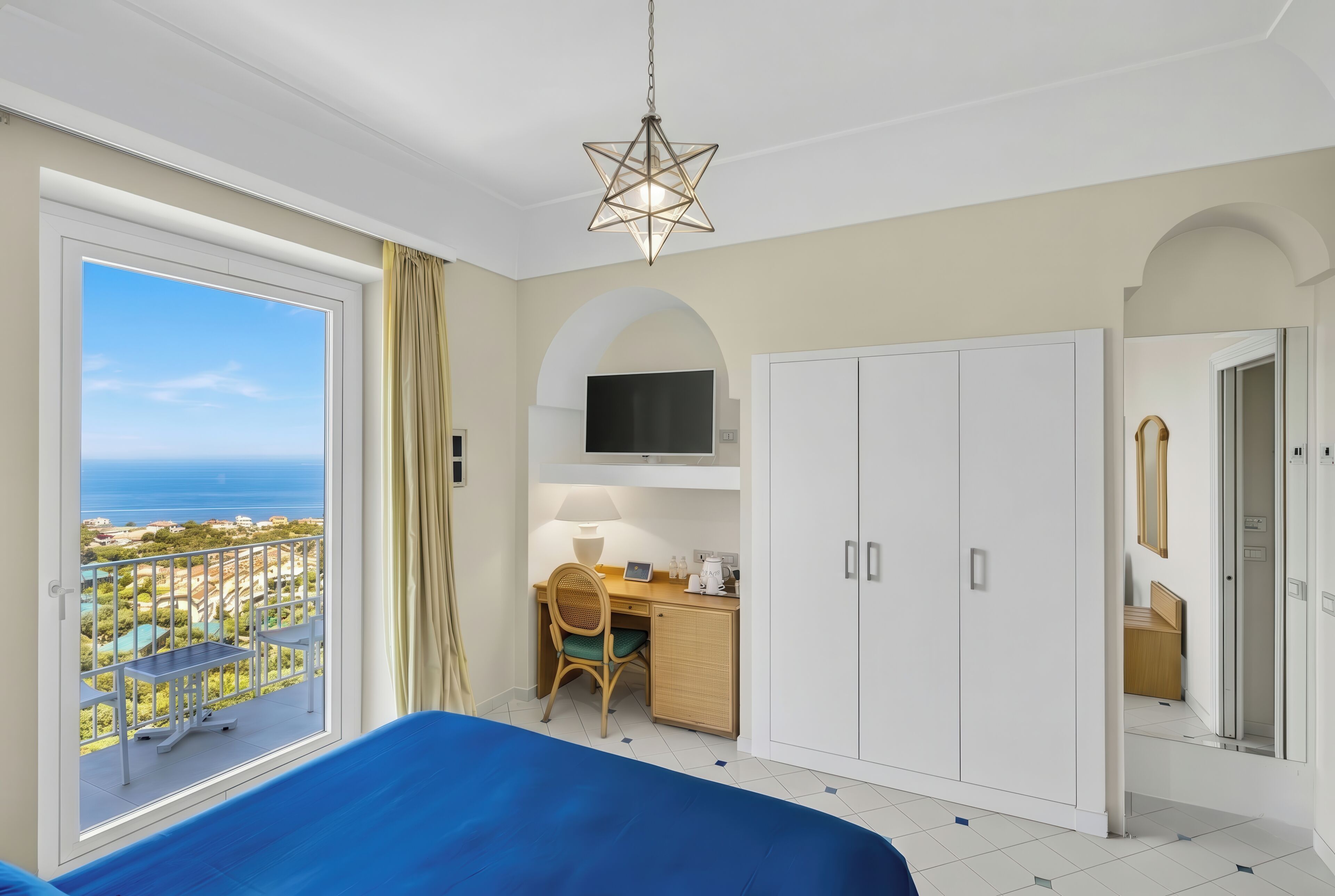 Een slaapkamer met een bed, bureau, kledingkast, televisie en een balkon met uitzicht.