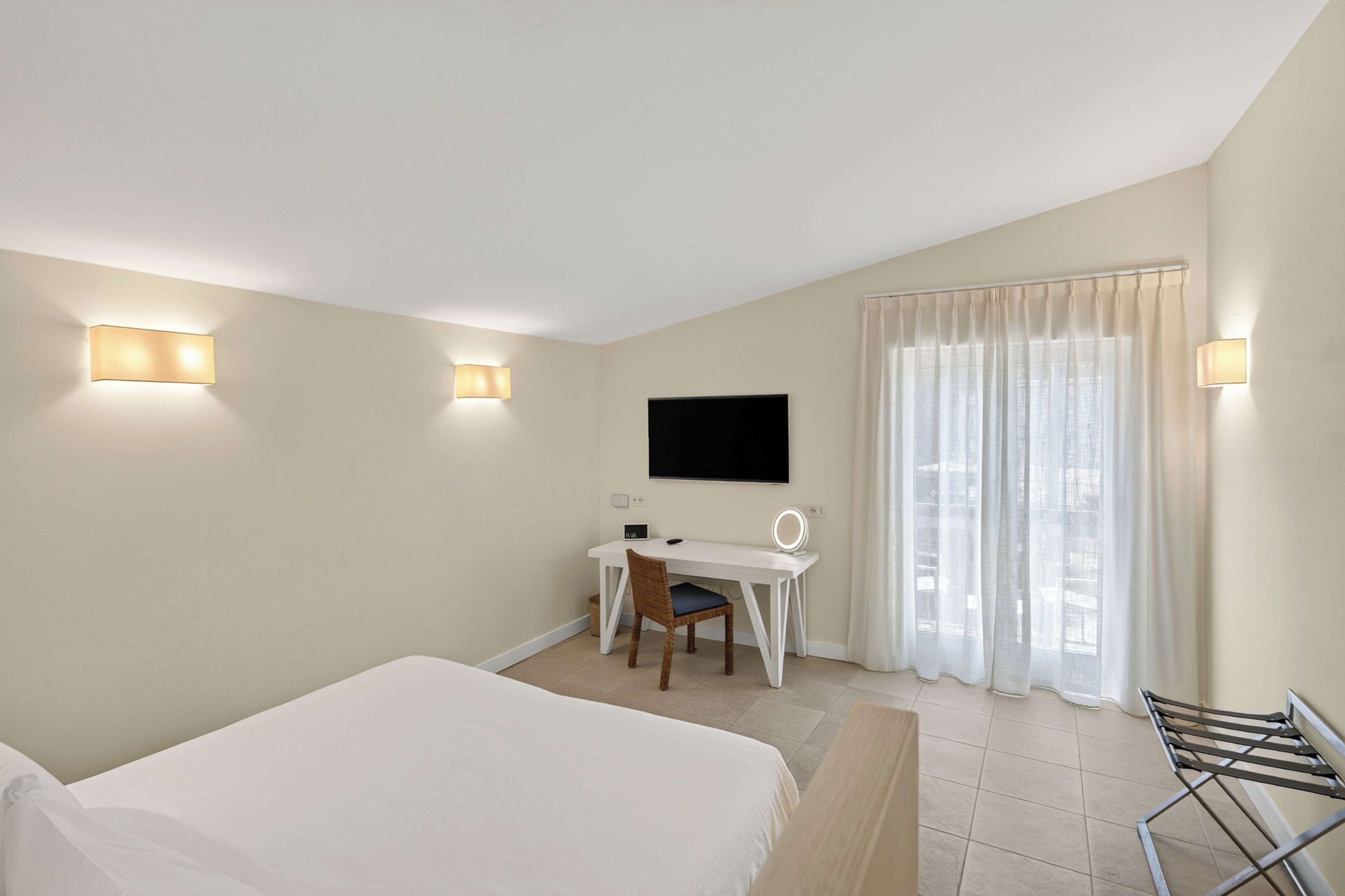 A hotel room with a bed, a desk, a chair, a TV, and a window with curtains.